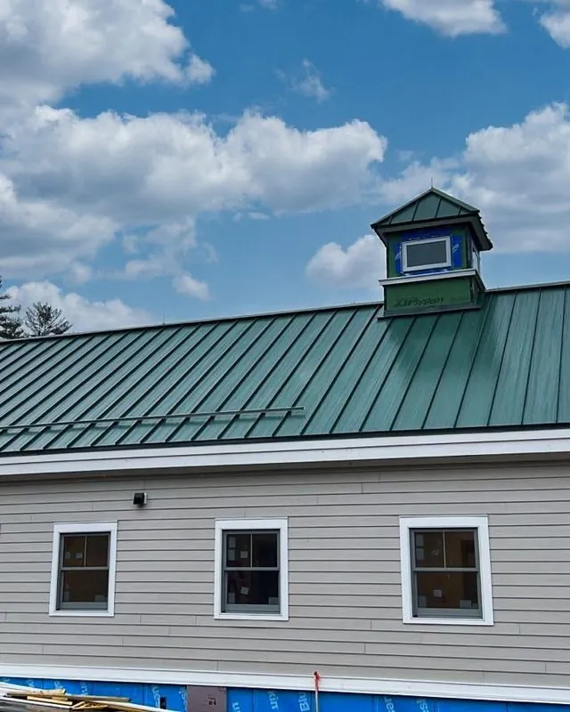 Long home with a green standing seam roof and cupola
